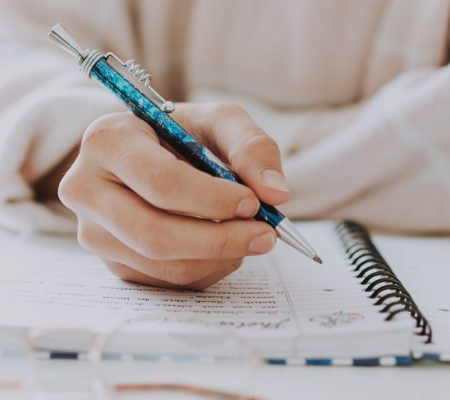 A vertical selective closeup of a female writing in a notebook with a blue pen